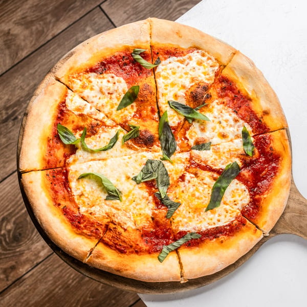 Hampton Junction's Margherita pizza, sliced and garnished with fresh basil on a wooden board.