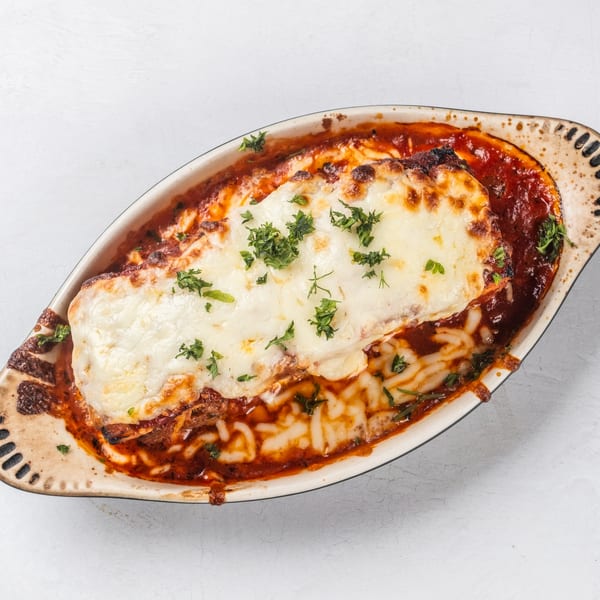Hampton Junction's baked lasagna with melted cheese and parsley in a rustic oval dish.