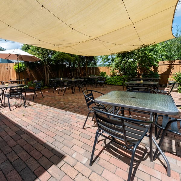 Hampton Junction's outdoor patio with brick flooring, black tables, chairs, and a large shade canopy.
