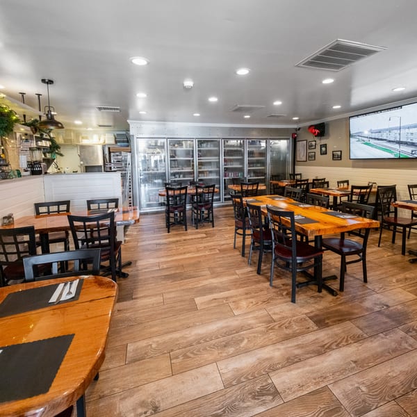 Empty Hampton Junction dining room with wooden tables, black chairs, and large refrigerators in the background.